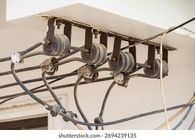 Close-up of multiple old electrical insulators and black power cables mounted on a wall for overhead utility connection