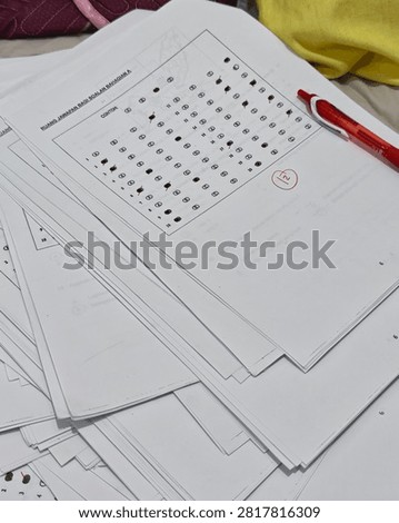 Close-up of multiple optical mark recognition (OMR) answer sheets stacked on a desk with a red pen, representing school examinations, academic assessment, testing, grading and education.
