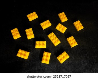 Close-up of multiple small yellow building blocks resembling classic LEGO pieces arranged randomly on a black textured surface. Ideal for creative construction concepts and toy themes.