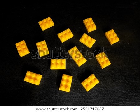 Close-up of multiple small yellow building blocks resembling classic LEGO pieces arranged randomly on a black textured surface. Ideal for creative construction concepts and toy themes.