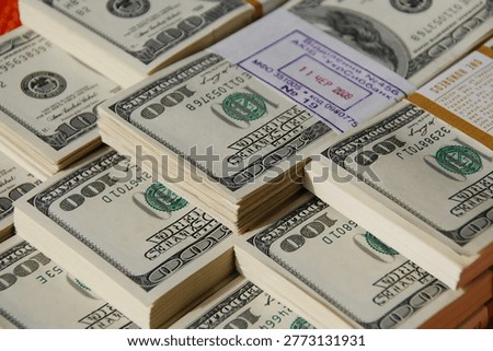 Close-up of multiple stacks of US one hundred dollar bills arranged in piles, secured with a bank band and stamp. The image highlights cash, finance, wealth, and banking concepts with detailed texture and sharp focus.
