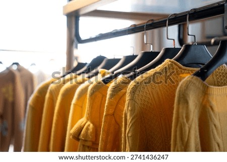 Close-up of multiple yellow knitted sweaters hanging on clothing racks in a retail store