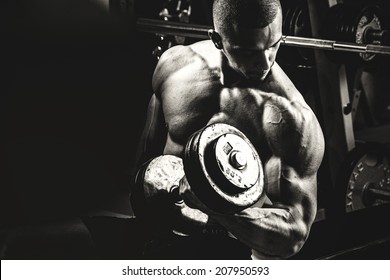 Closeup of a muscular young man lifting weights on dark background 