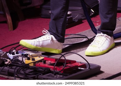 Close-up of a musician's feet operating guitar pedals during a live performance, emphasizing the interaction with the equipment. - Powered by Shutterstock