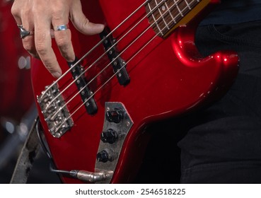 Close-up of a musician's hand playing a red electric bass guitar, showcasing details of the strings and instrument body during a live performance. - Powered by Shutterstock