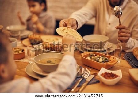 Close-up of Muslim father passing his son Lafah Bread during dinner at dining table on Ramadan.