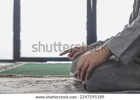 Close-up of Muslim man praying salat, proceeds to sit and recite the tashahhud, salawat with fingers movement at the mosque, 