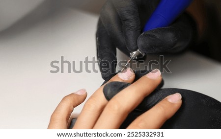 Close-up of nail master using tool to clean female clients nails in beauty studio. Worker wear protective black gloves for work. Care and beauty concept