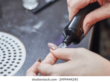 Close-up of a nail technician applying gel to a nail extension using a tube, in a professional nail salon. - Powered by Shutterstock