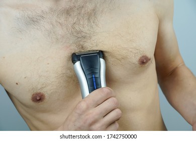 Close-up of a naked man using an electric razor to remove hair from his chest
