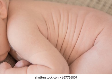 Closeup Of Naked Newborn Baby Sleeping In Fetal Position With Focus On The Upper Body Stomach Area Where The Skin Folds