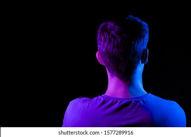 Close-up of the nape, back and shoulders of an short hair head of a man with stubble in shirt, illuminated on one side in blue and on the other pink on a black isolated background