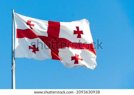 Close-up of the national flag of Georgia fluttering in the wind against a blue sky with copy space. Concept of international relations.