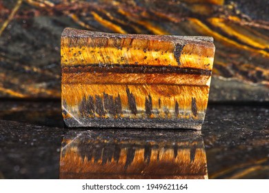 Close-up Of Natural Mineral Gem Stone - Tiger's Eye On Dark Polished Slab Opposite Another Tiger Eye Stones. Gemstone Tiger Eye With A Golden Color.