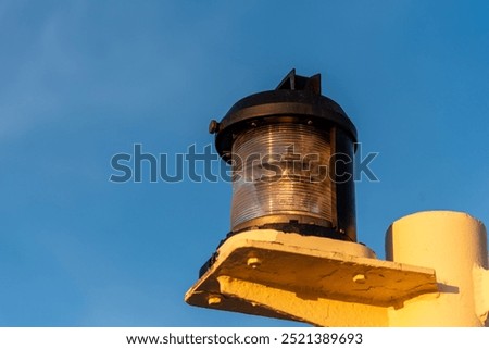 Close-up of navigation lights on a large cargo ship, the lamps standing out sharply against the clear blue sky. The detail captures the essential maritime equipment.