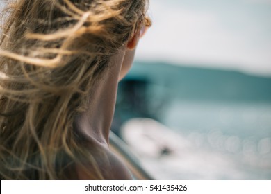 Closeup of neck of a girl looking something in the distance with wind in her hair. Woman body part on the beach - focus on the neck. Anonymous, no visible face.