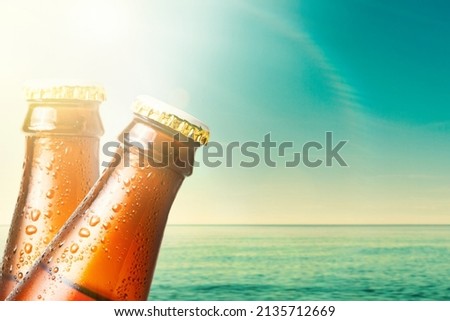 Close-up of the necks of two wet glass bottles of dark beer against the background of the ocean and the sky. Copy space. Alcoholic beverages on vacation.