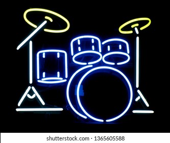 A closeup of a neon drum set sign on display in a business window