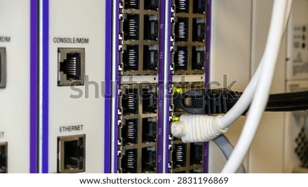 Close-up of a network switch panel showing multiple RJ45 ports, console and ethernet connections, with black and white patch cables plugged in and green activity LEDs glowing.
