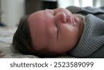 Close-up of a newborn baby’s face scrunching up while sleeping, highlighting the delicate features and natural expressions of infancy in a cozy and warm environment