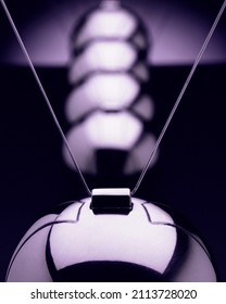 Close-up of Newton pendulum with 5 balls of metal in action from front against dark background	