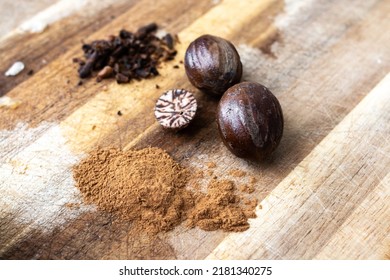 Close-up of nutmeg in its raw form on a wooden chopping block in Grenada.  Includes ground nutmeg, a cross-section of a nutmeg, chopped cloves in the background, and raw nuts. Spice island, Caribbean.