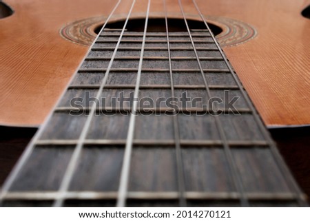 Close-up of old acoustic guitar fretboard with selective focus in the center. Neck perspective with blurred soundhole and strings. Music concept