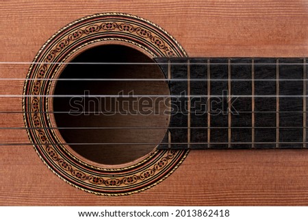 Close-up of old acoustic guitar showing detail of decorative rosette decal around soundhole, strings and part of ebony fretboard. Top down view flat lay with music concept