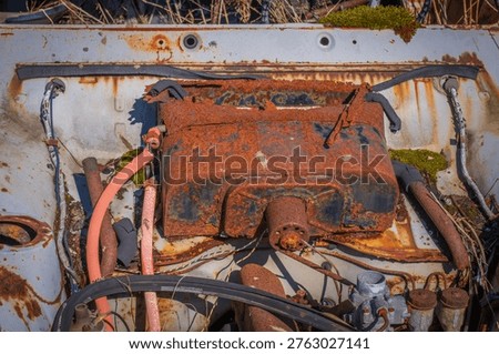 Closeup of old car engine compartment with heavy rust, hoses and mechanical parts decaying over time.