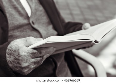 Closeup Of An Old Caucasian Man Reading A Book Outdoors, In Black And White