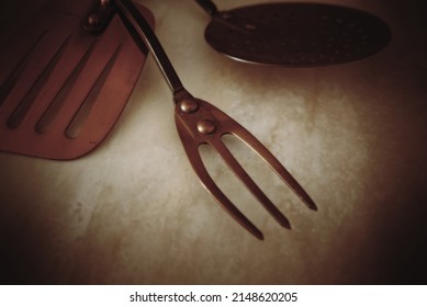 closeup of old copper cooking fork, with two other utensils on a marble countertop.