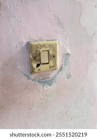 A close-up of an old and damaged light switch on a wall. The switch plate is discolored and cracked, showing visible signs of wear and tear. The surrounding wall has peeling paint and moisture damage.