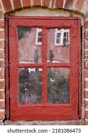 Closeup Of An Old Dirty Window In A Red Brick Home. Zoom In On Casement With Red Wood Frame On A Historic Building With Bumpy Paint Texture. Macro Exterior Details Of Windowsill In A Traditional Town