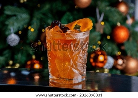A closeup of old fashion cocktail served in a glass against a Christmas tree
