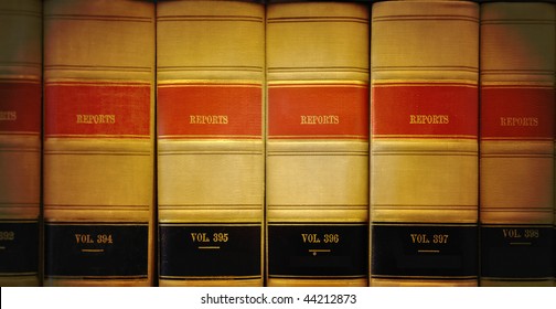 A closeup of old looking law books in a library on a shelf. The lighting is on the center. Colors are brown, red and black.