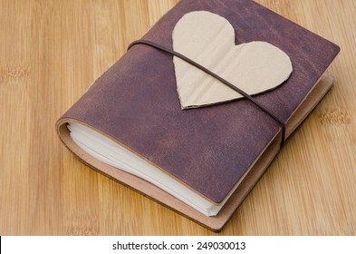 closeup of an old notebook with a cardboard heart on top on a wooden table