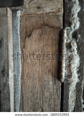 Close-up of an old rusty metal hinge on a weathered wooden door.