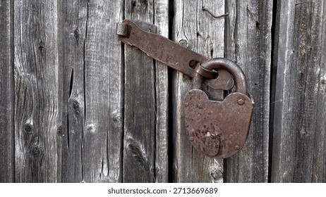 A close-up of an old, rusty padlock securing a weathered wooden door, showcasing the texture of the aged wood and the corroded metal.