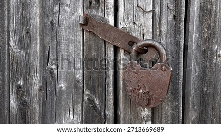 A close-up of an old, rusty padlock securing a weathered wooden door, showcasing the texture of the aged wood and the corroded metal.