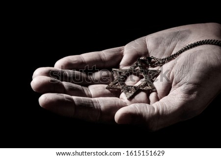 closeup of an old and rusty pendant in the shape of the star of david on the hand of a man