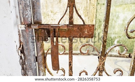 Close-up of old rusty slide bolt latch on vintage wrought iron gate. Vintage rusty iron bolt lock on old metal gate with moss and peeling paint.