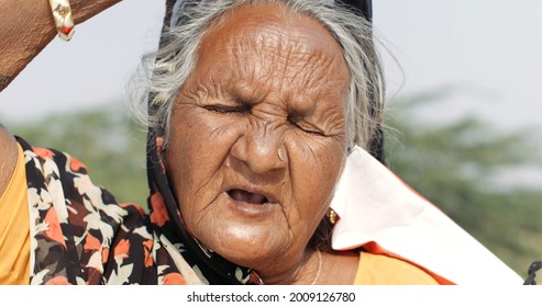 A Closeup Of An Old South Asian Woman With Her Eyes Closed And A Covid Mask Dangling From One Ear