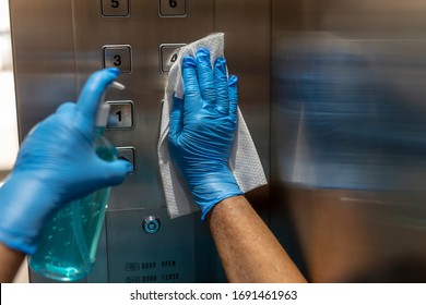 Closeup of old staff hand using wet wipe cleaning an elevator push button control panel with a blue sanitizer bottle.Disinfection,cleanliness and healthcare,Anti Corona virus,COVID-19.Selective focus.