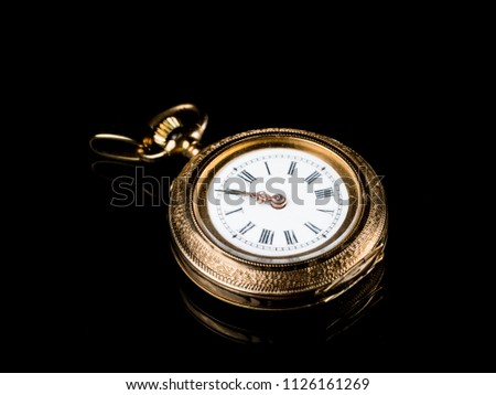 Closeup of an old, used golden pocket watch on a black reflective surface