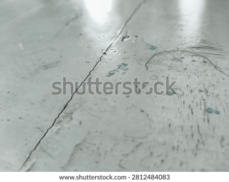 Close-up of an old, weathered gray tabletop with a long crack, fine scratches, a small rust stain, blue ink marks and dried teal glue droplets, worn texture background
