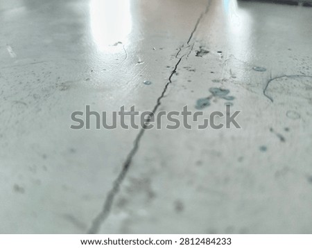 Close-up of an old, weathered gray tabletop with a long crack, fine scratches, a small rust stain, blue ink marks and dried teal glue droplets, worn texture background
