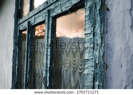 Close-up of an old weathered window with peeling paint and lace curtain in warm sunset light. moldova