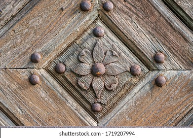 Close-up of an old wooden door decorated with carved wood made flowers with corroded and rusty fittings.