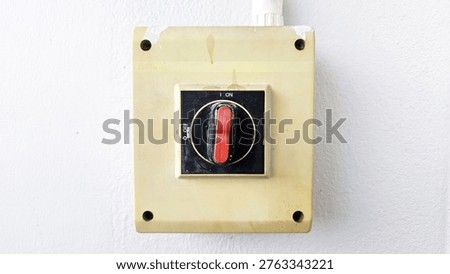 A close-up of an old, yellowed electrical switch panel on a white wall with a red toggle in the 