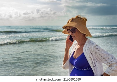 Close-up Of Older Woman On The Shore Of The Beach Talking On Her Smartphone. Concept Of Summer Family Vacation.